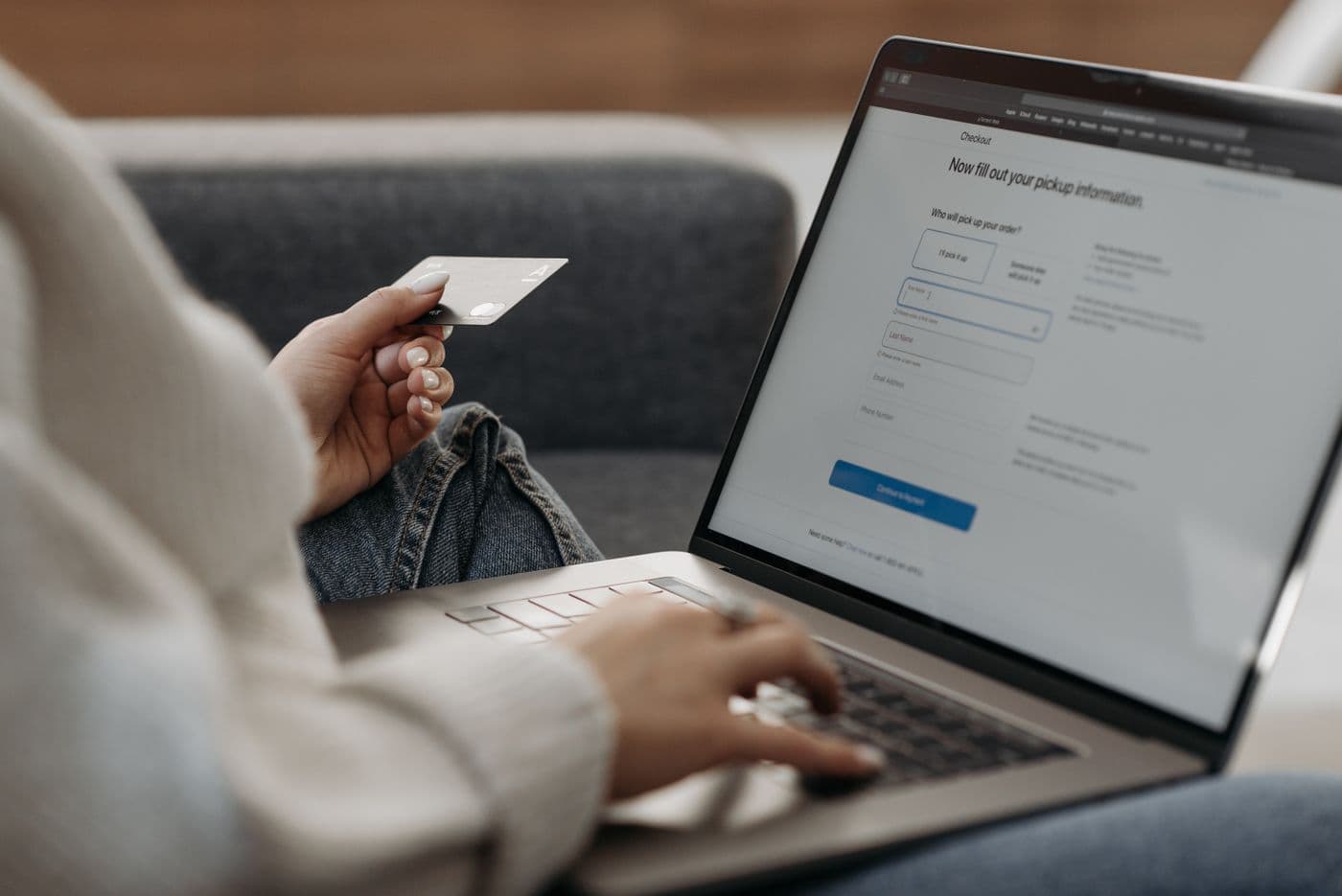 Tangan memegang kartu kredit di depan laptop yang menampilkan halaman checkout belanja online
